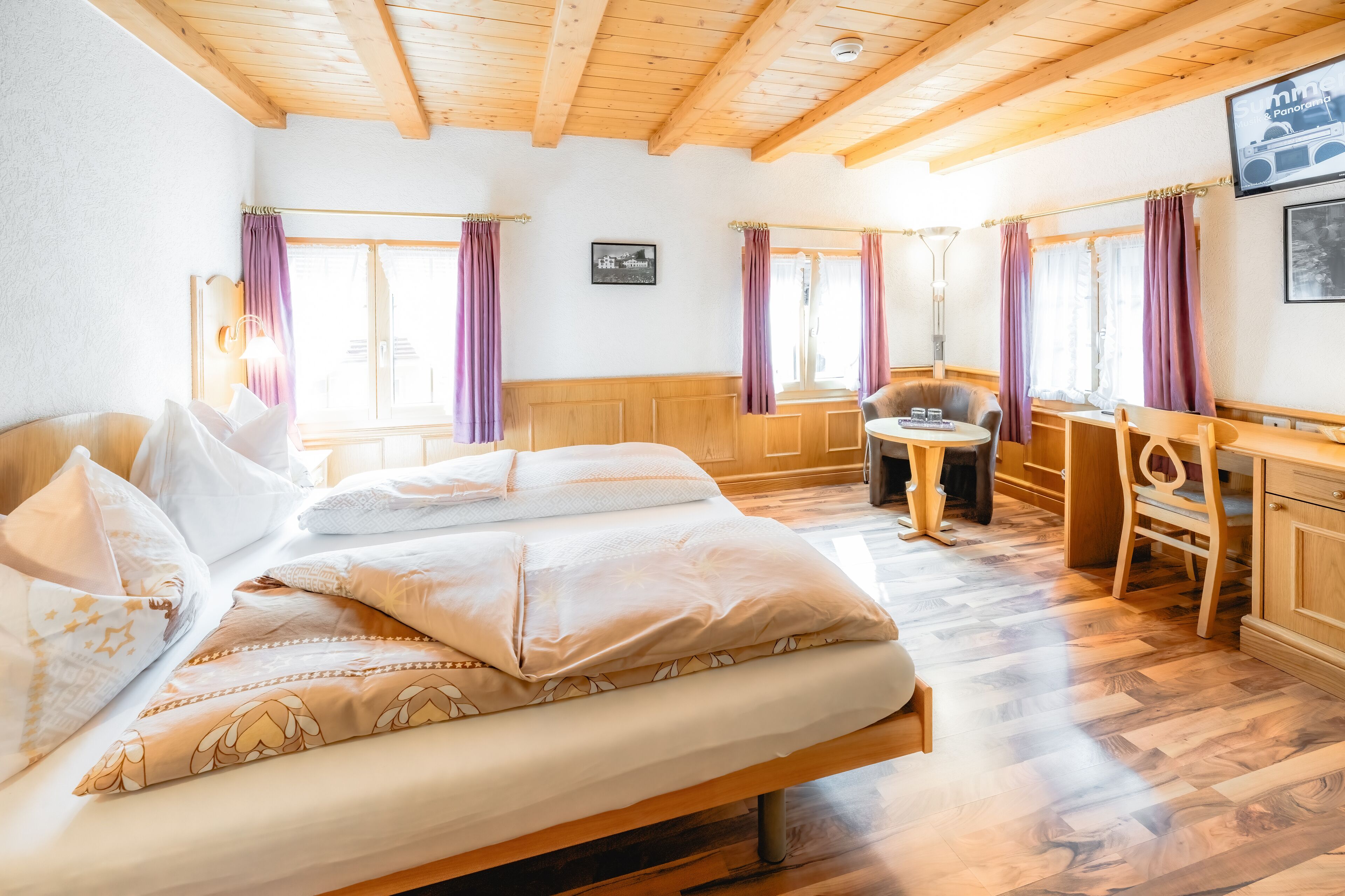 A room with a bed, a desk, and a chair. There are curtains on the windows, and a picture is on the wall.