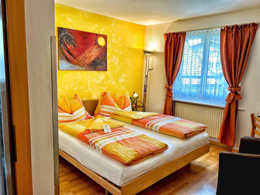 A room with a bed, a painting on the wall, a lamp, and a window with curtains.