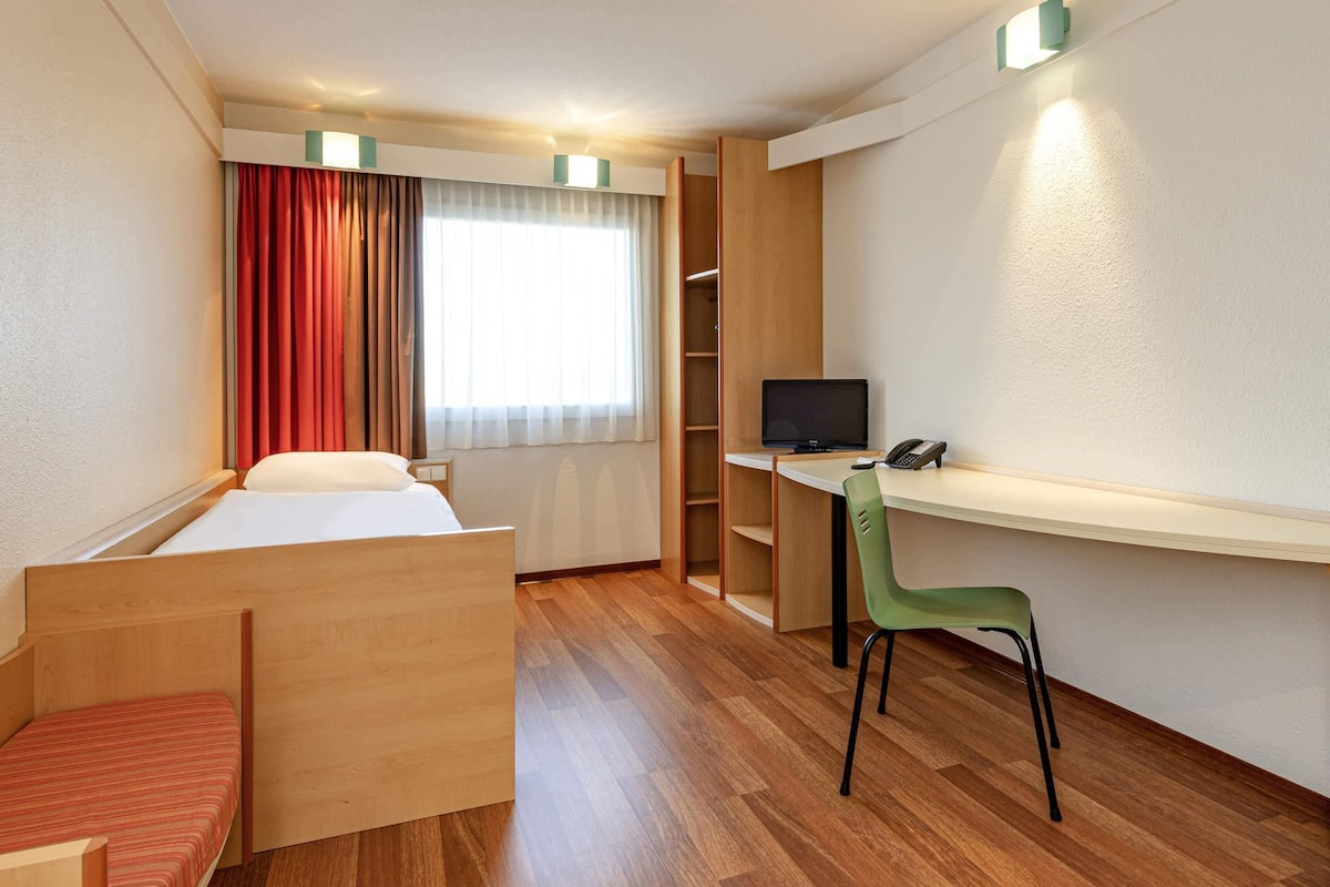 Une chambre d’hôtel comprenant un lit, un bureau avec une chaise, une télévision et un téléphone.