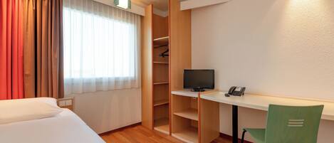 A hotel room with a bed, a desk with a computer, a chair, a wardrobe, and a telephone.