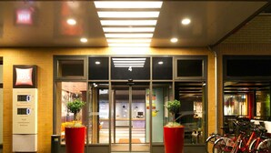 The exterior of a hotel with a prominent 'ibis Hotels' sign, a glass entrance, and a red planter with a small tree. - ibis Berlin City Potsdamer Platz (Berlin)
