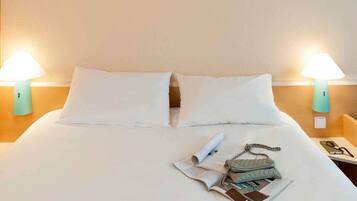 A neatly made bed with white linens, two bedside lamps, and a small table with a book and a handbag.