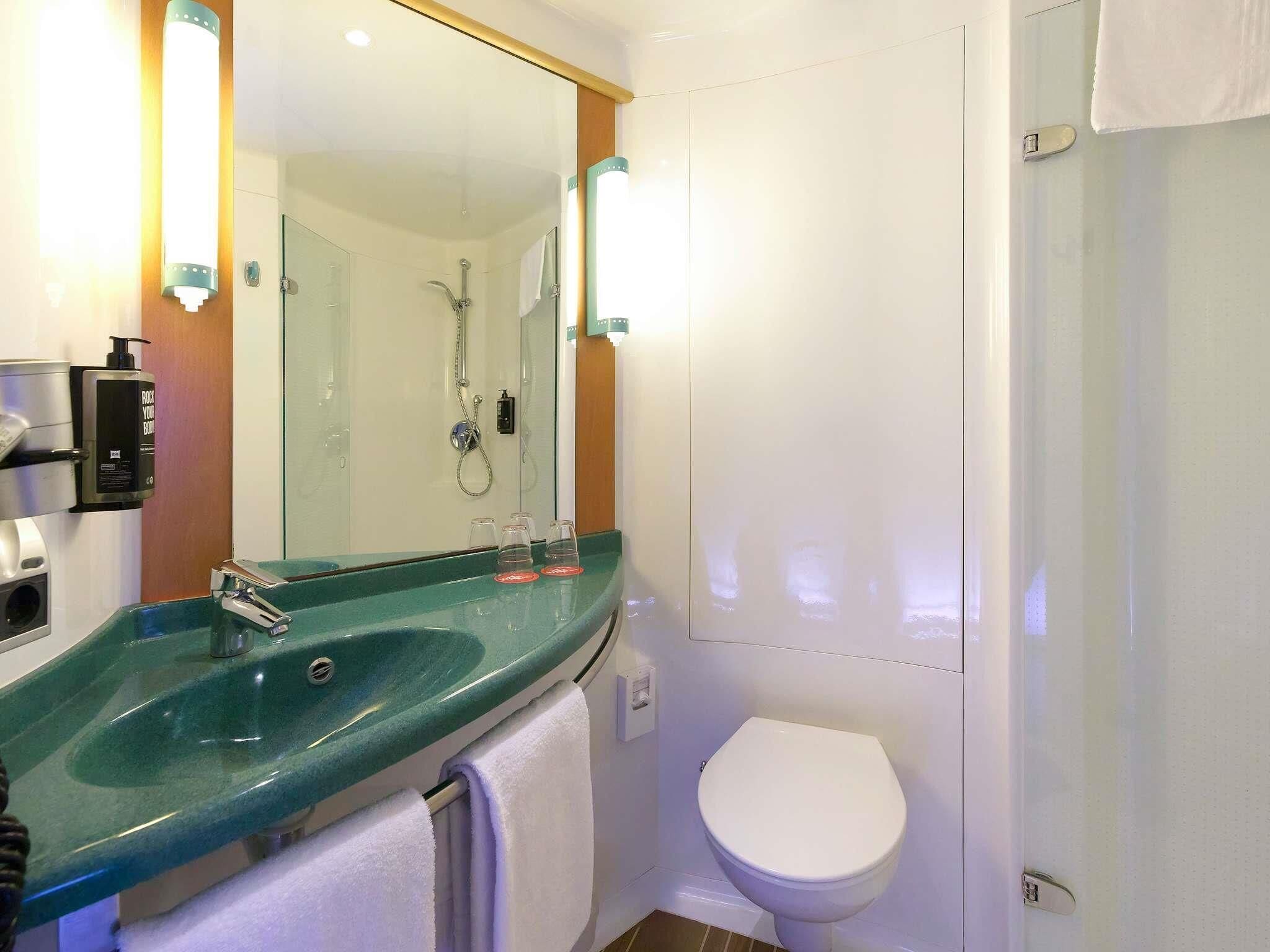 A bathroom with a glass sink, a white toilet, and a shower.