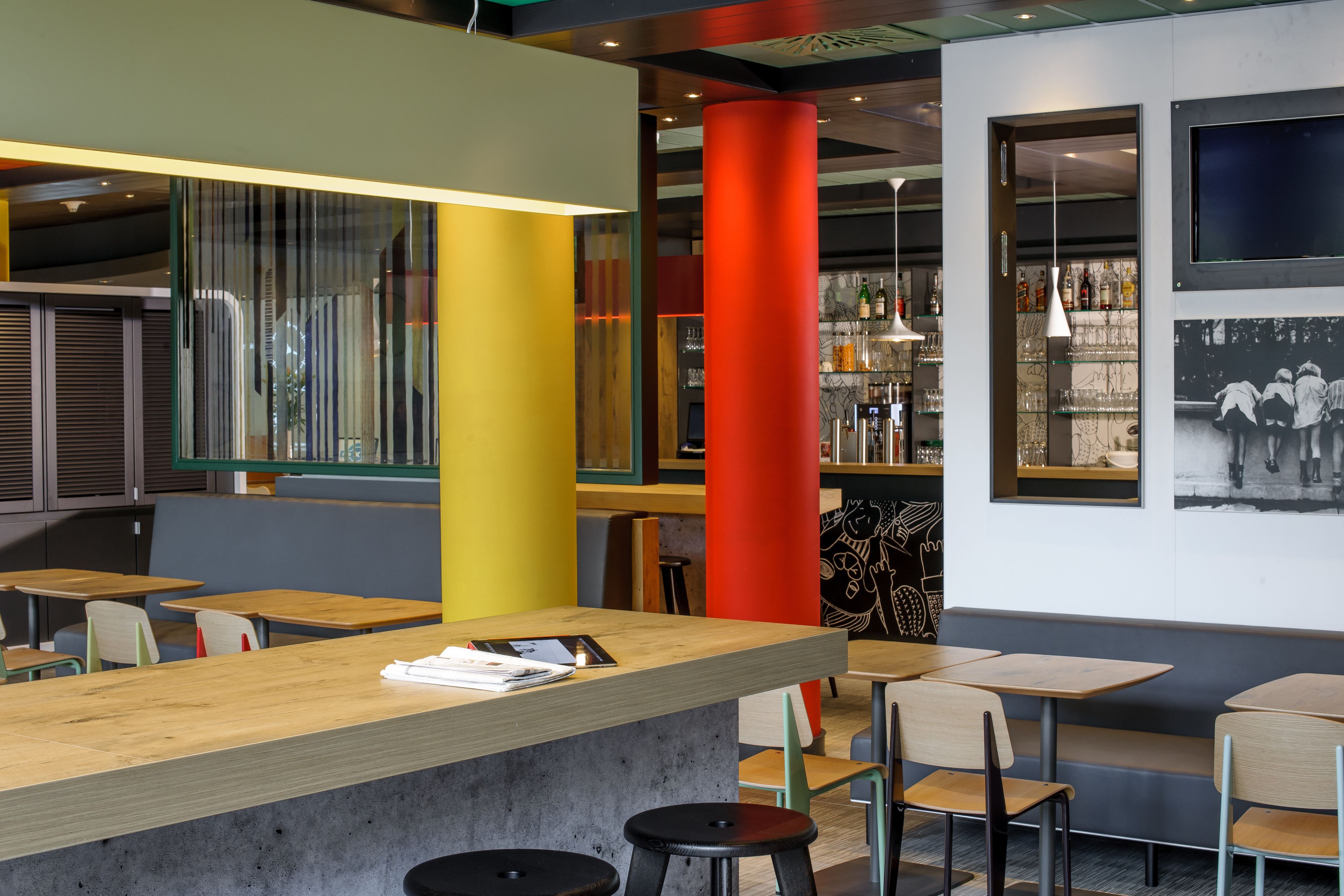 A modern bar area with wooden tables and stools, a concrete counter, and a bar stocked with bottles.