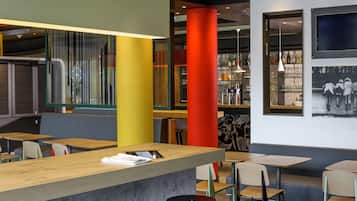 A modern bar area with wooden tables and stools, a concrete counter, and a bar stocked with bottles.