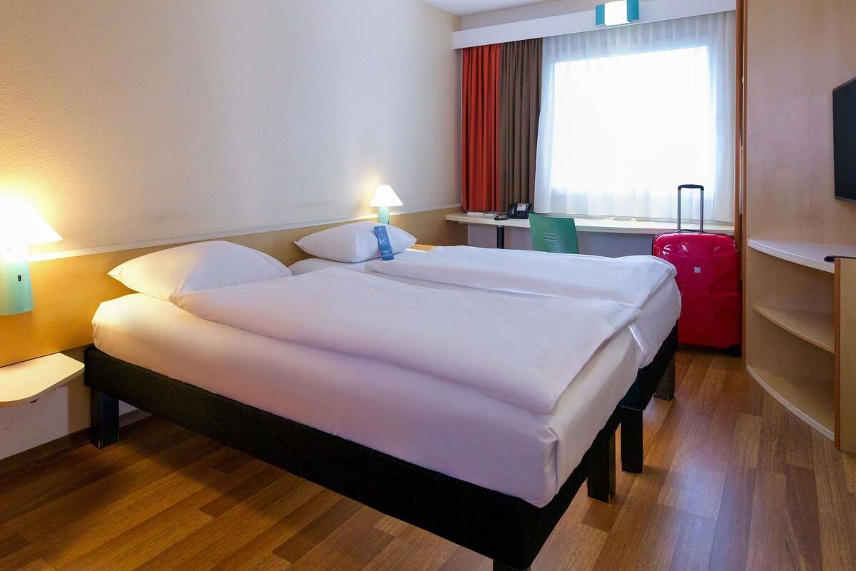 Une chambre d’hôtel avec un lit double, des tables de chevet, un bureau, une chaise, une télévision et une fenêtre avec des rideaux.