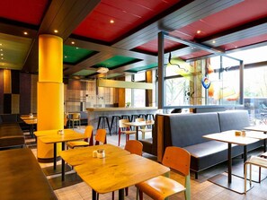 Un intérieur de restaurant moderne avec des tables et des chaises en bois, un bar et un coin salon avec un canapé.