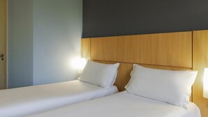 Habitación de hotel con dos camas individuales, cabecero de madera y lámparas de noche.