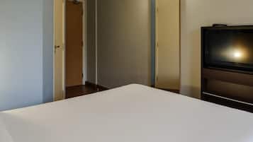 Habitación de hotel con cama, televisor, puerta y lámpara fijada a la pared.