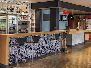 A bar area with a wooden counter, black chairs, and a patterned wall. - ibis Curitiba Aeroporto (Sao Jose dos Pinhais)