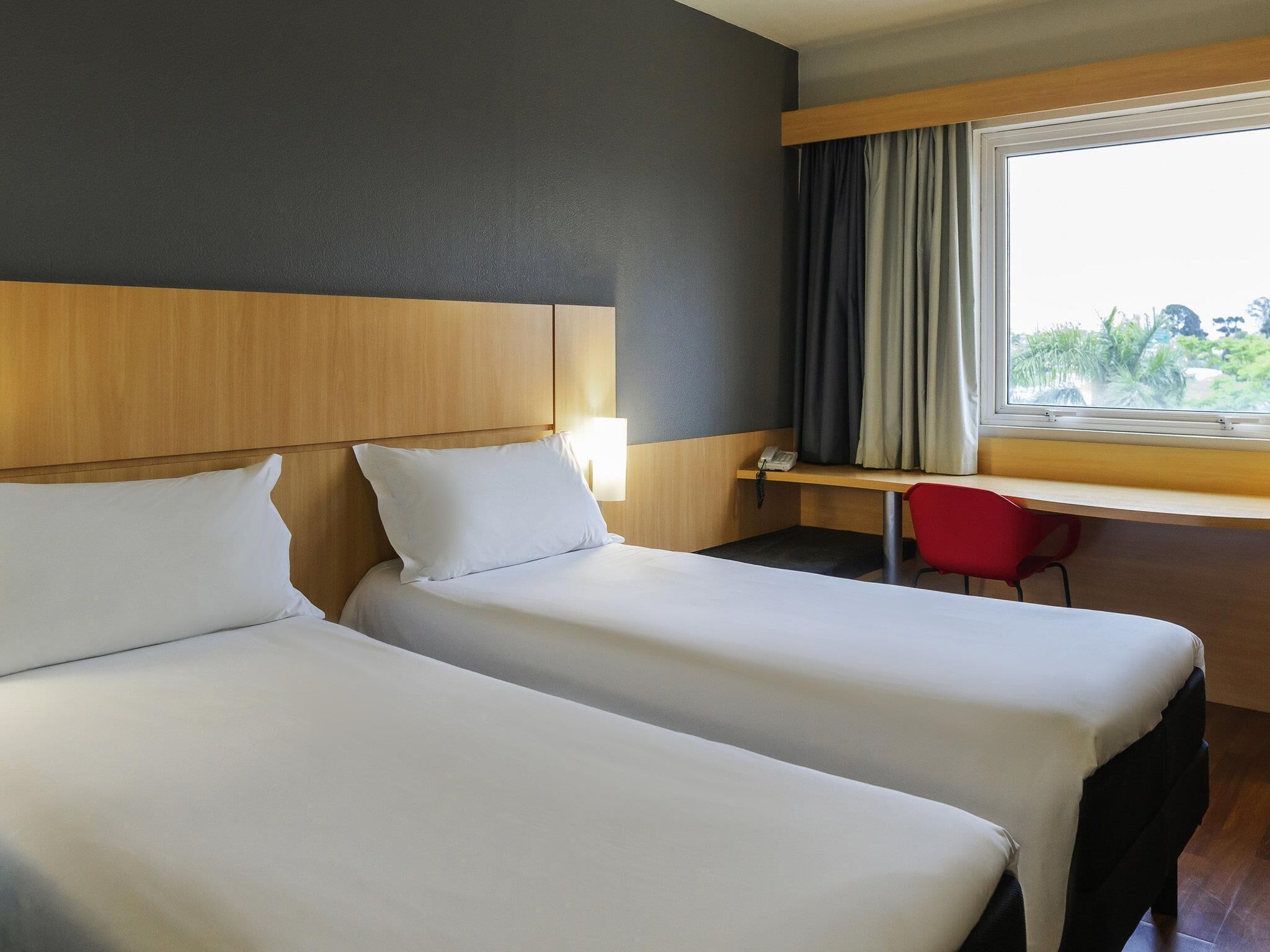 Ein Hotelzimmer mit zwei Betten, einem Schreibtisch, einem Stuhl und einem Fenster mit Vorhängen.