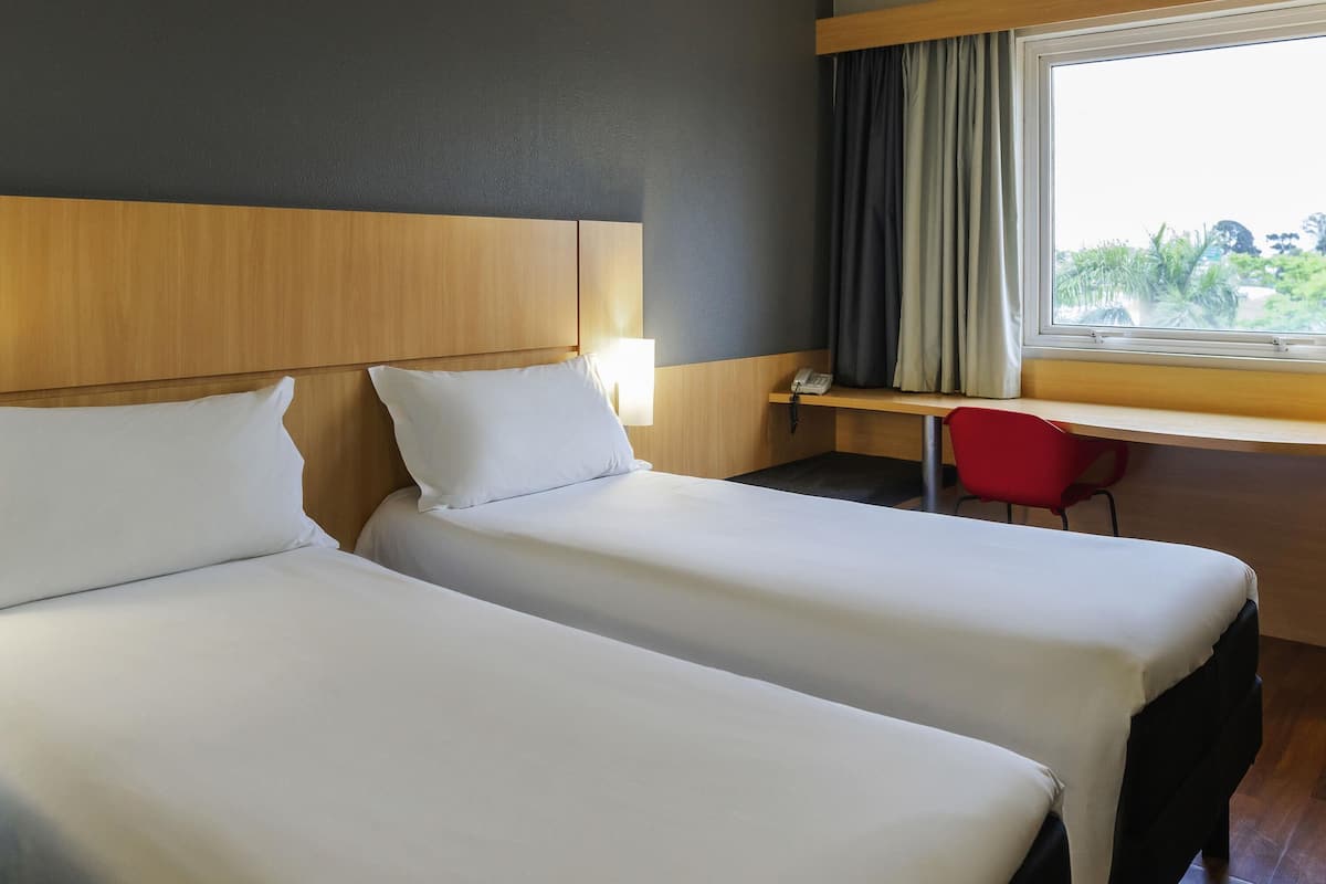 Habitación de hotel con dos camas, un escritorio, una silla, un teléfono y una ventana con cortinas.