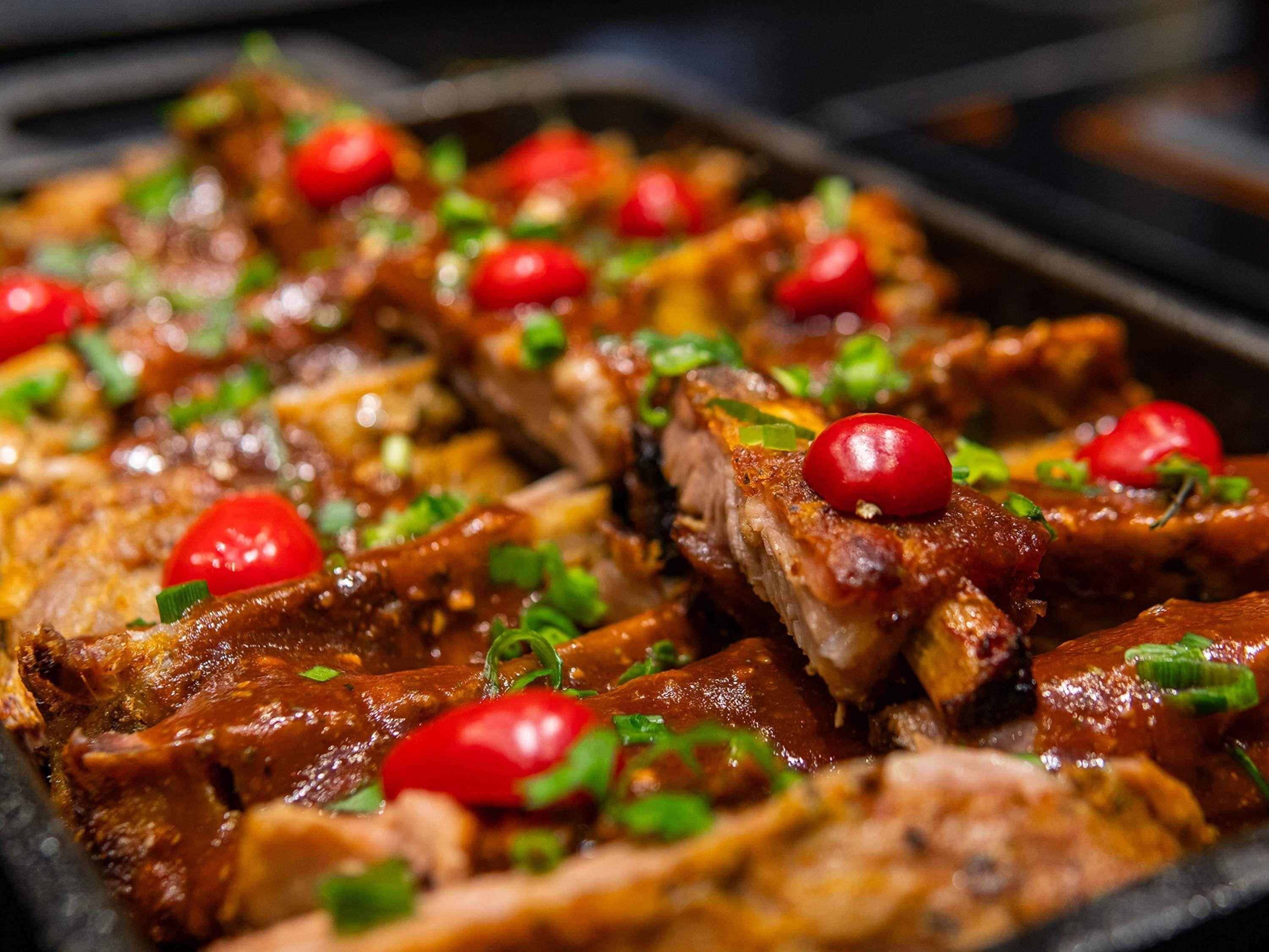 A close-up of sliced meat with a glossy sauce, garnished with cherry tomatoes and green herbs.