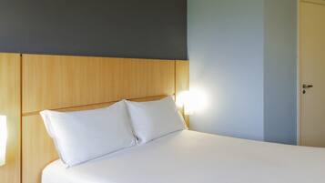 Una cama con ropa de cama blanca, un cabecero de madera y una mesita de noche con una lámpara.