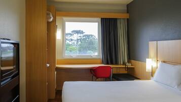 Una habitación de hotel con cama, escritorio, silla, televisión y ventana con cortinas.