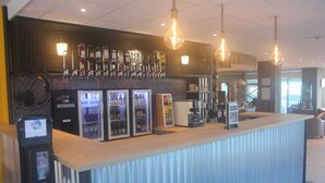 Een bar met verschillende drankflessen, een kassa en een koffieapparaat.