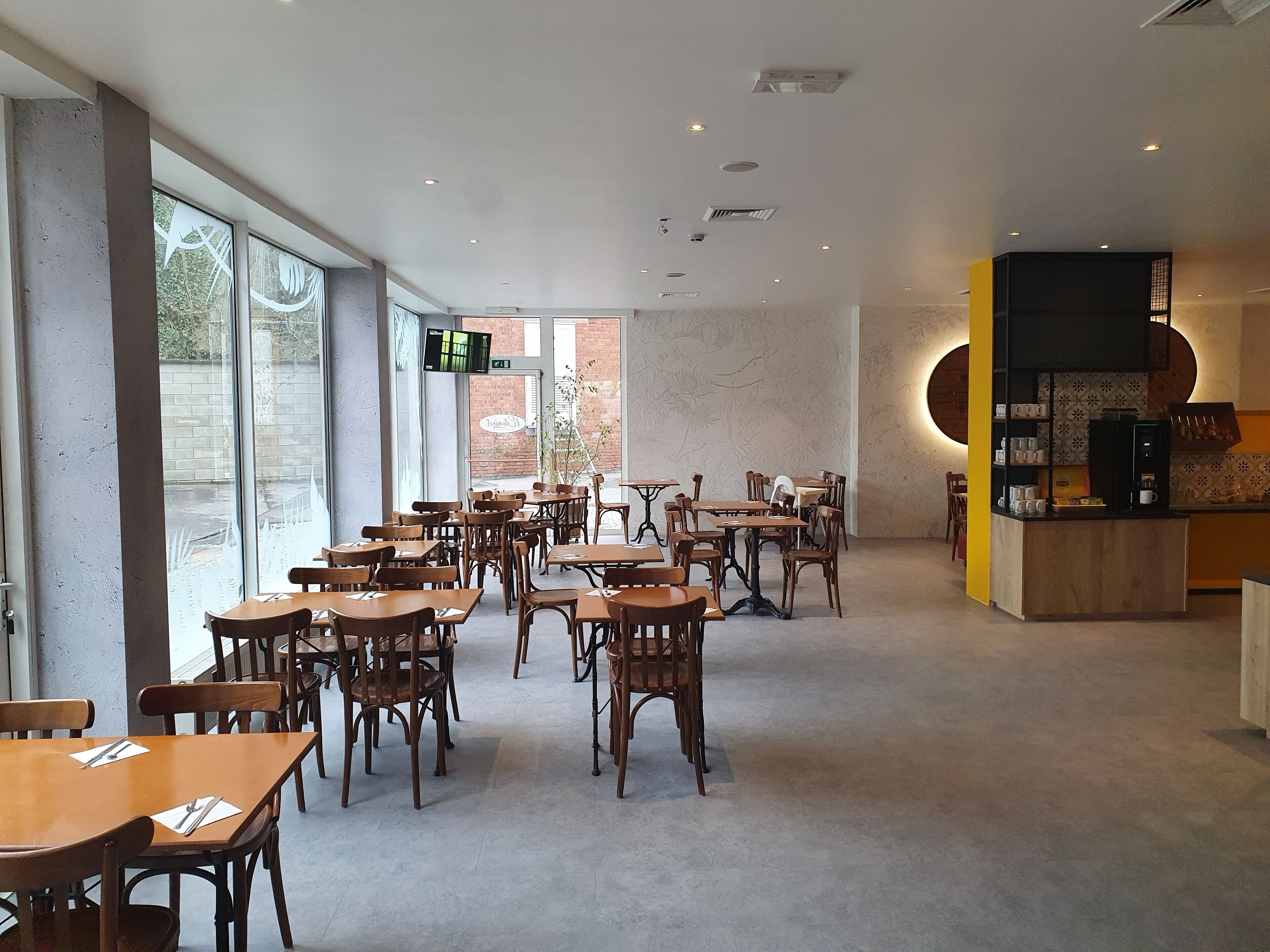 A spacious cafe with wooden tables and chairs, large windows, and a modern interior design.