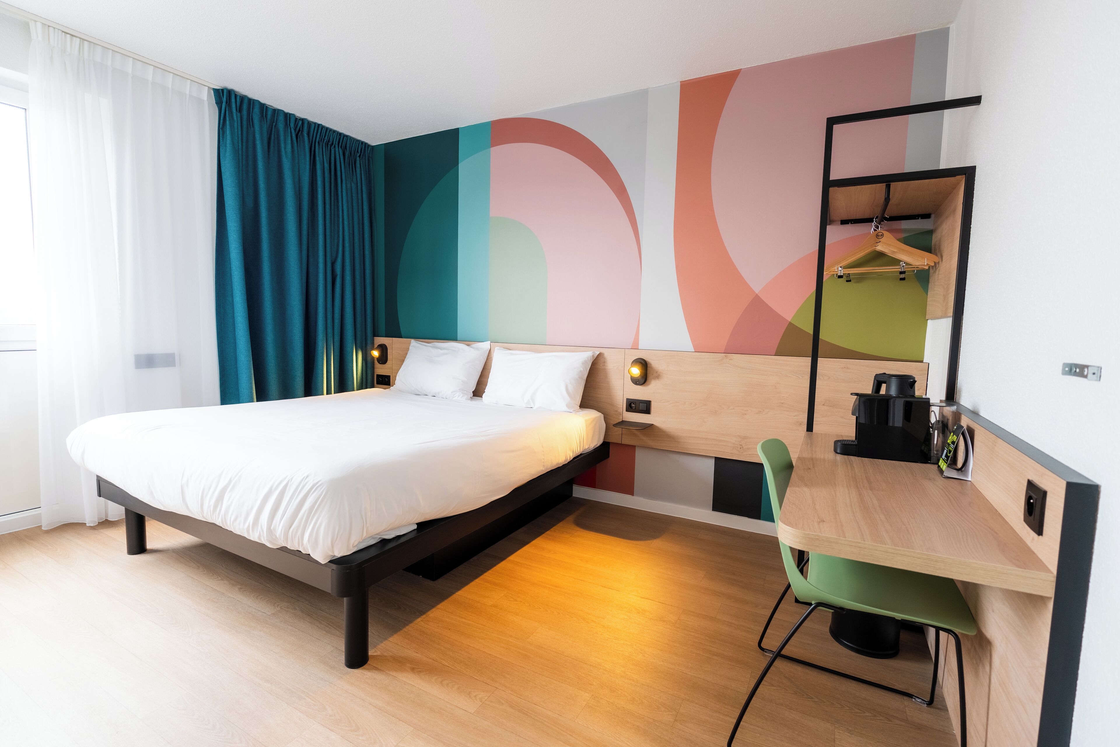 A modern hotel room with a bed, a desk, and a chair.