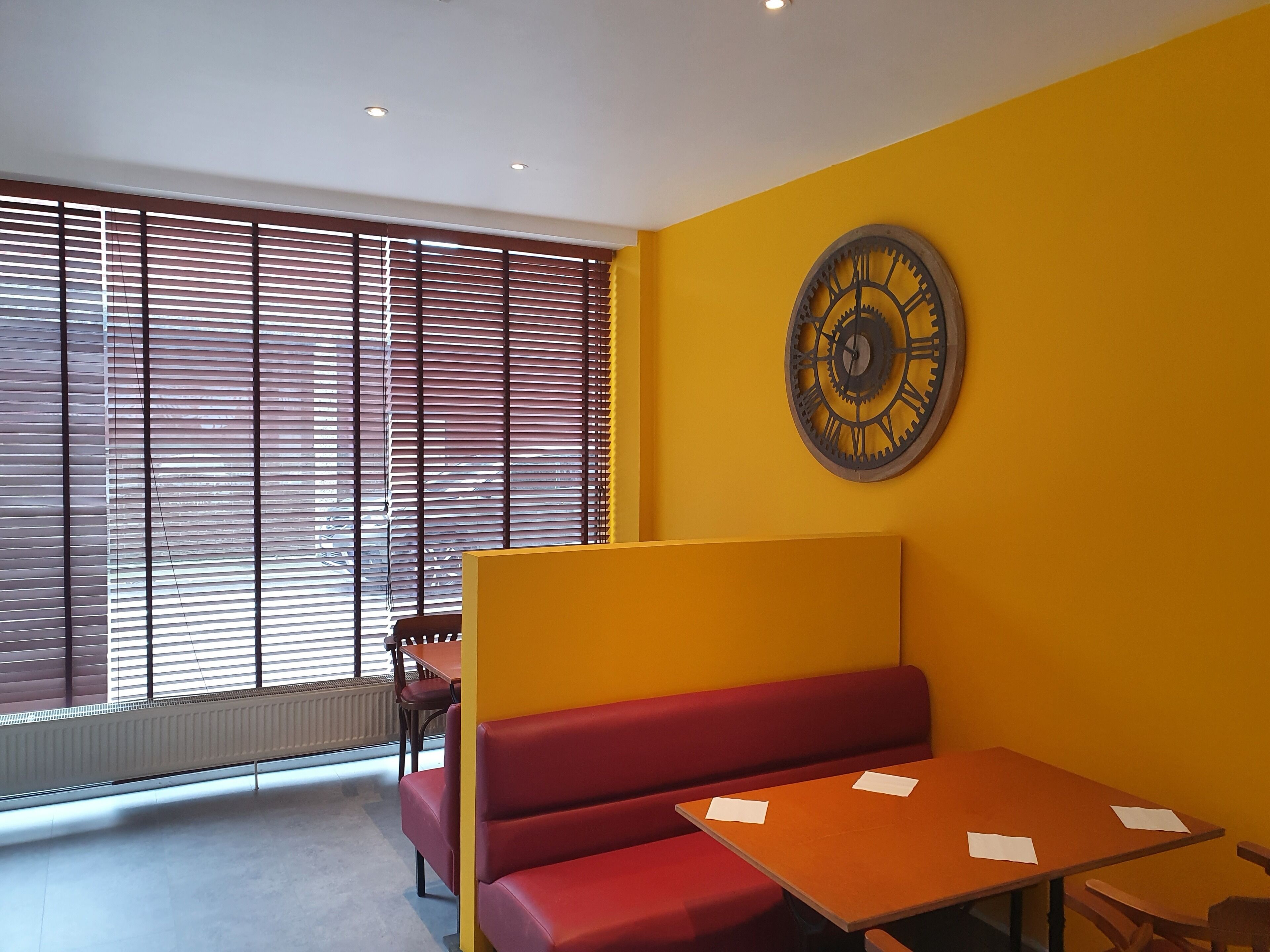 Una habitación con un banco rojo, una mesa de madera y un gran reloj de pared.
