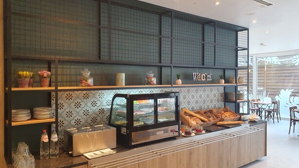 Een bakkerijbalie met een vitrine, planken met borden en een 'Welcome'-bord.