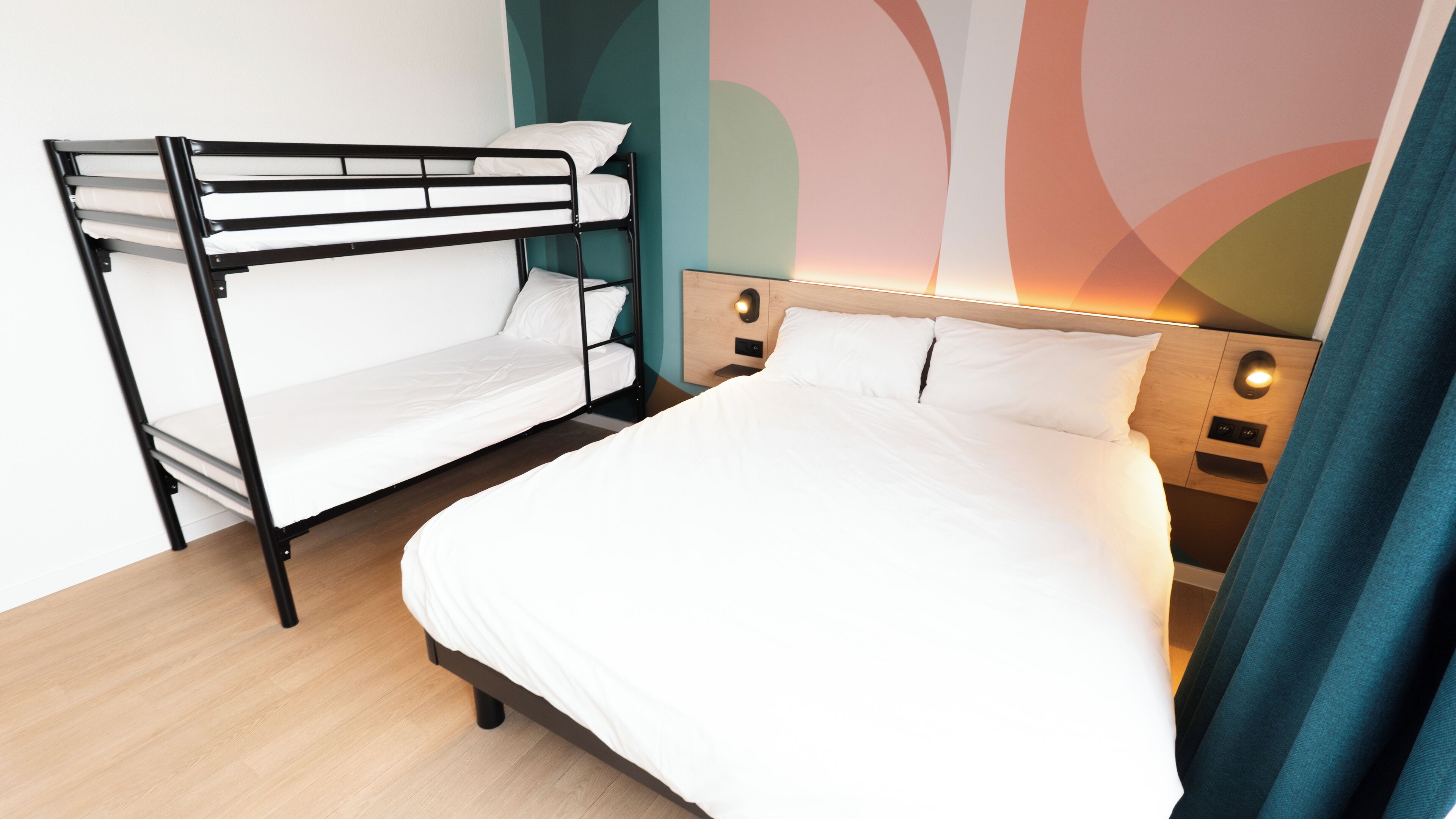 A bunk bed with white bedding and a single bed with white bedding in a room with teal and pink wall art.