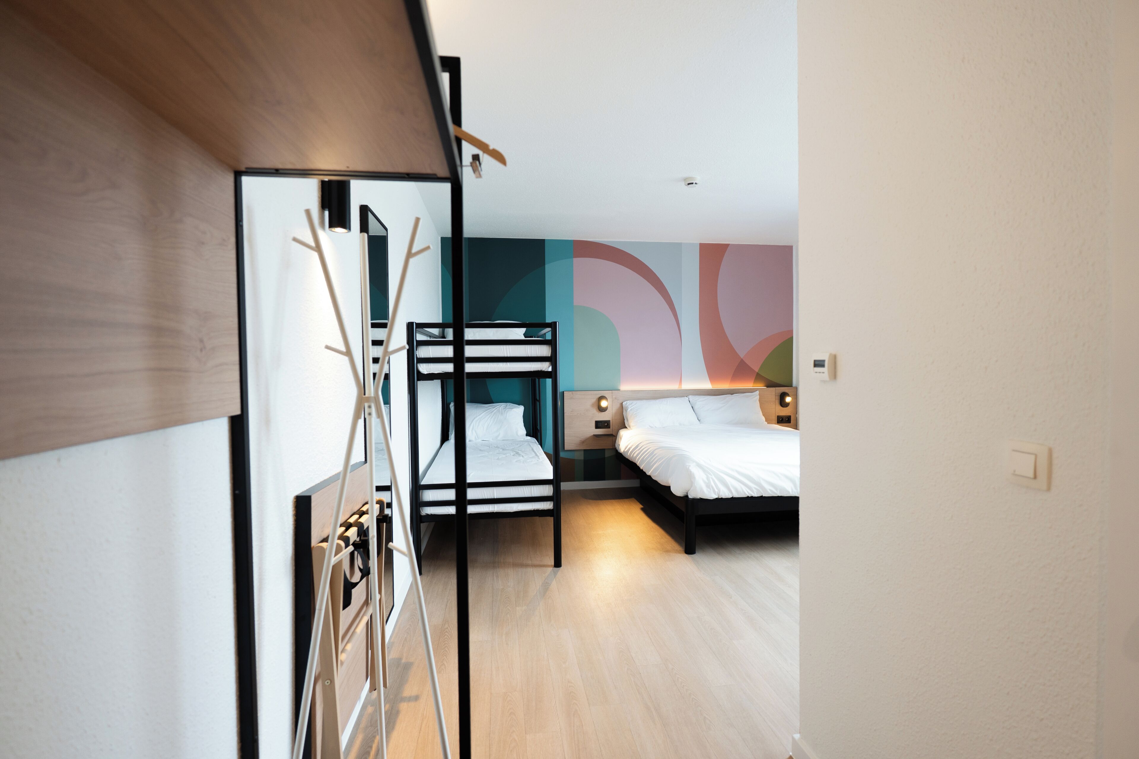 Una habitación de hotel moderna con una cama litera, un escritorio y un gran mural abstracto en la pared.
