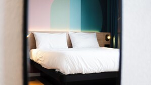 Een moderne hotelkamer met een net opgemaakt bed, een houten hoofdbord en een muur met een geometrisch ontwerp.