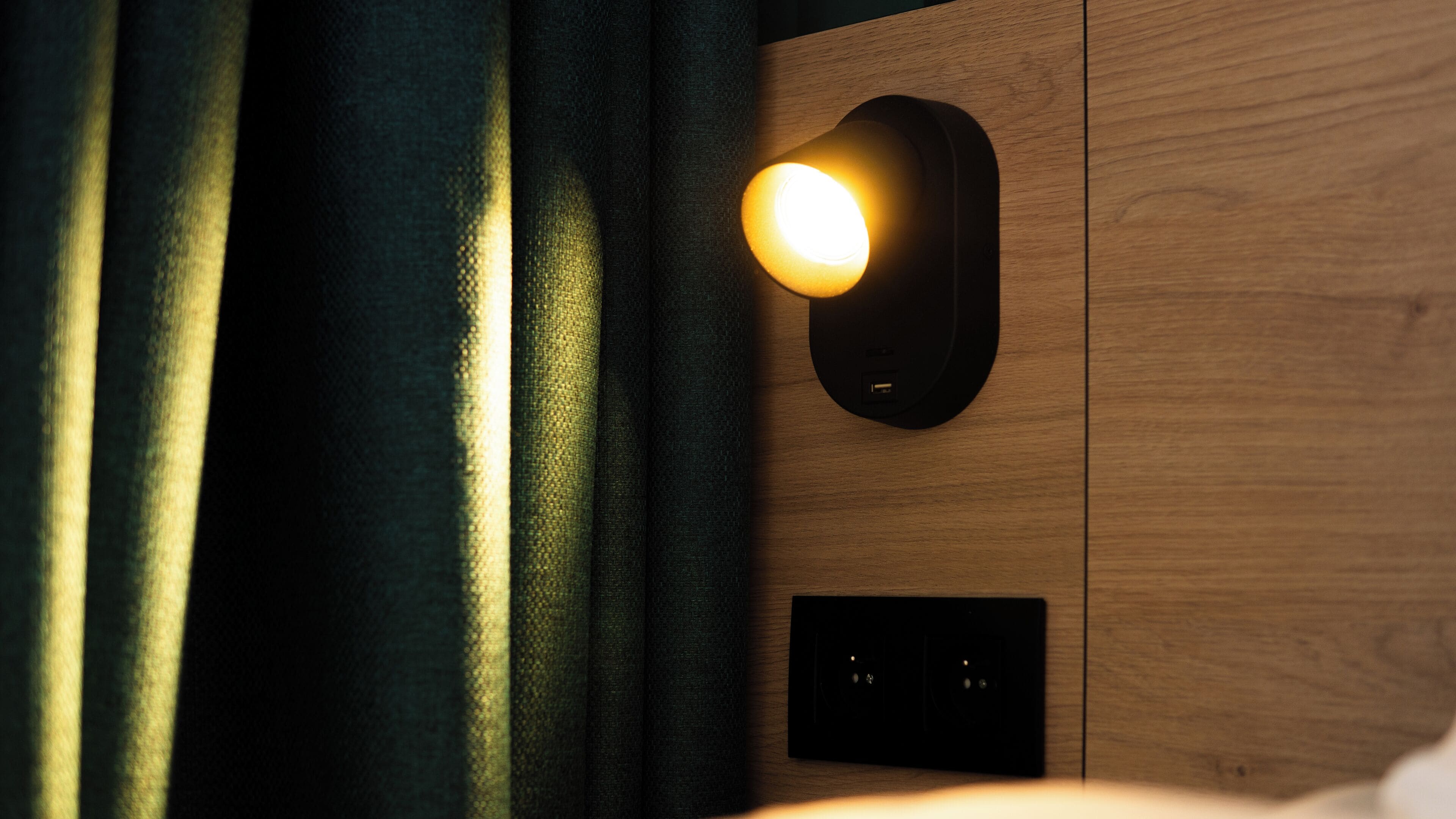 A wall-mounted light fixture with a glowing bulb, a power outlet, and a switch on a wooden panel.