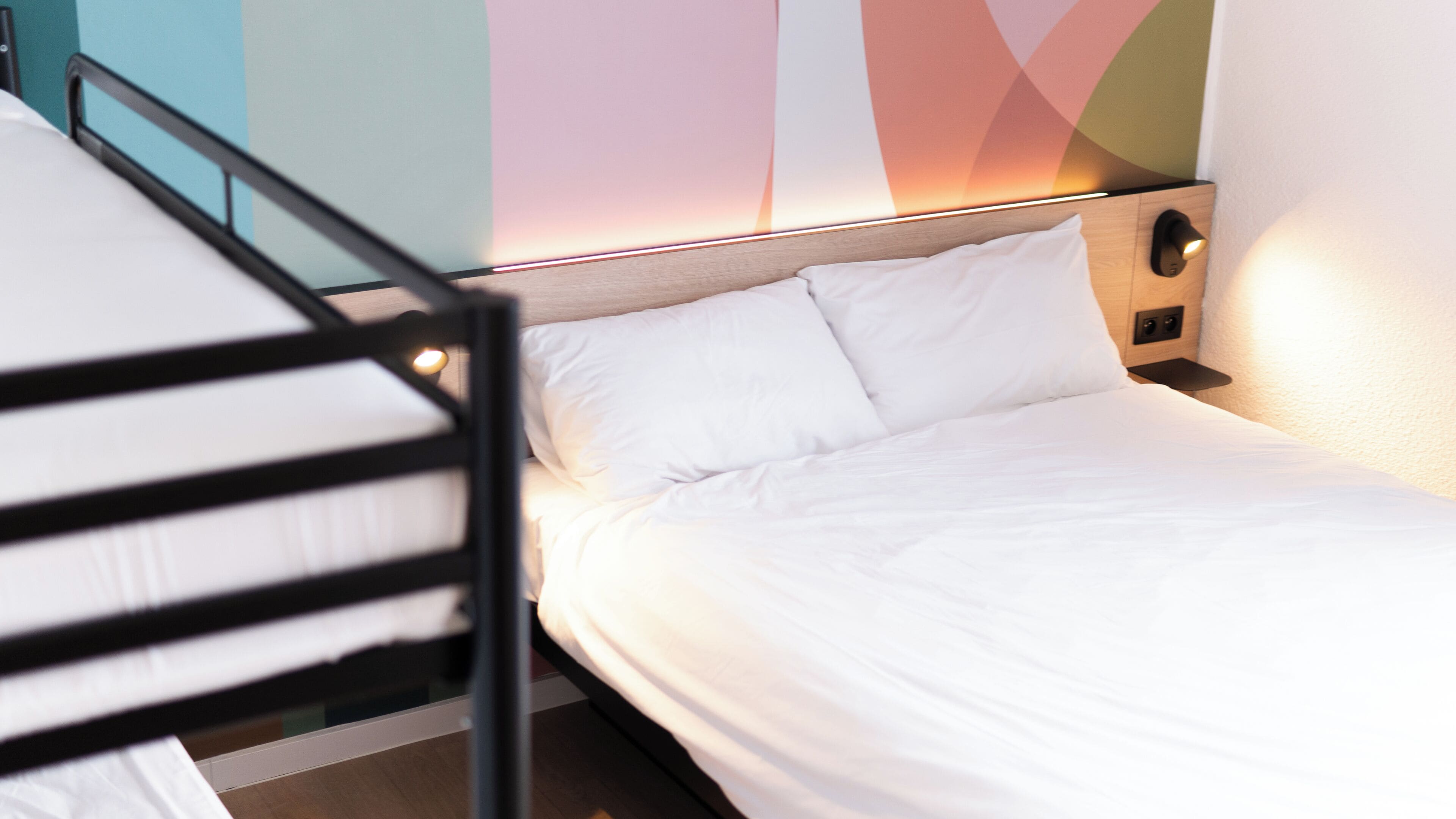 Un lit simple avec une literie blanche, dans une chambre au design moderne, comprenant une tête de lit en bois et un mur orné de motifs géométriques.