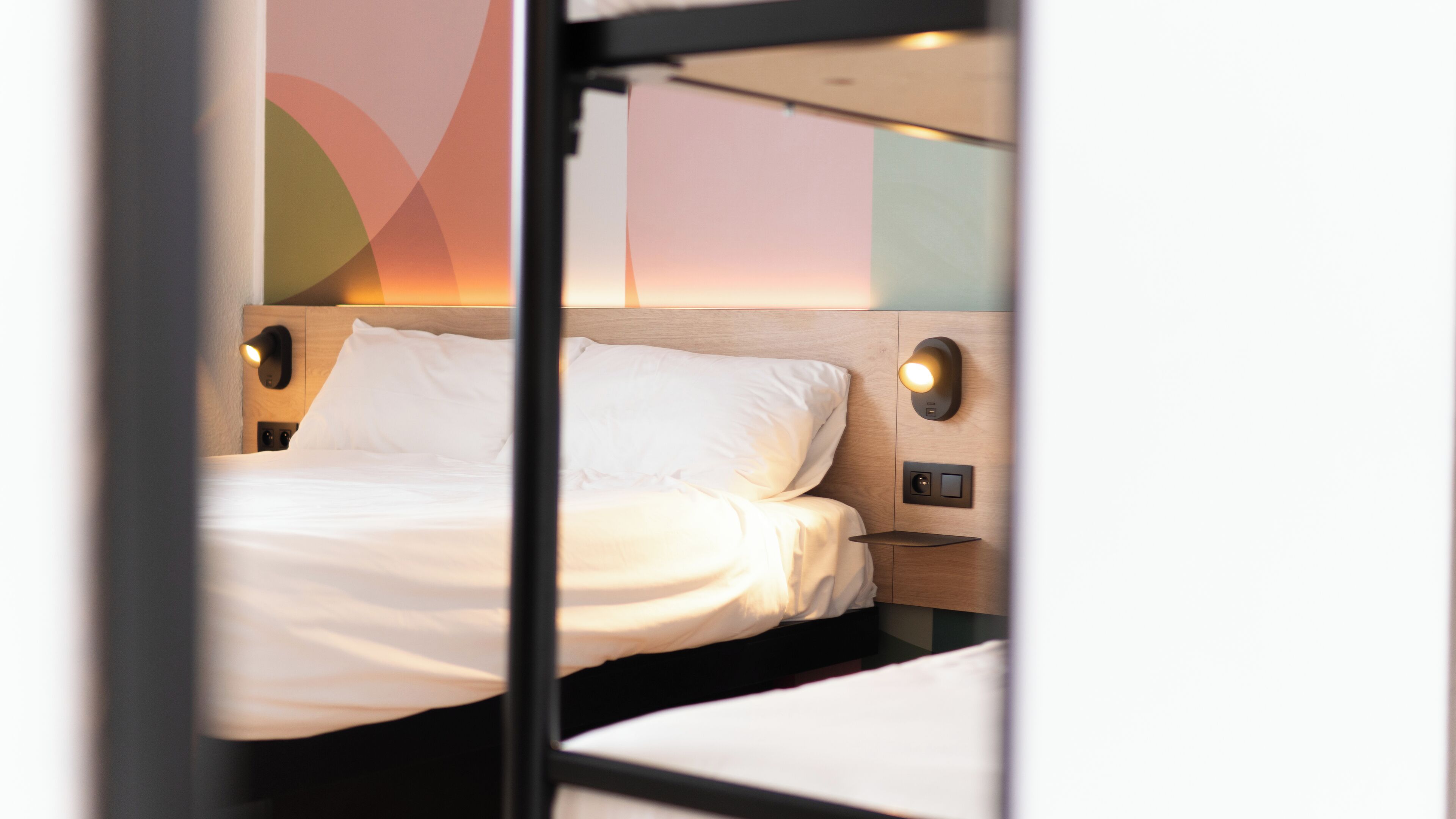 Een net opgemaakt bed met witte lakens, een houten hoofdbord en twee bedlampjes.