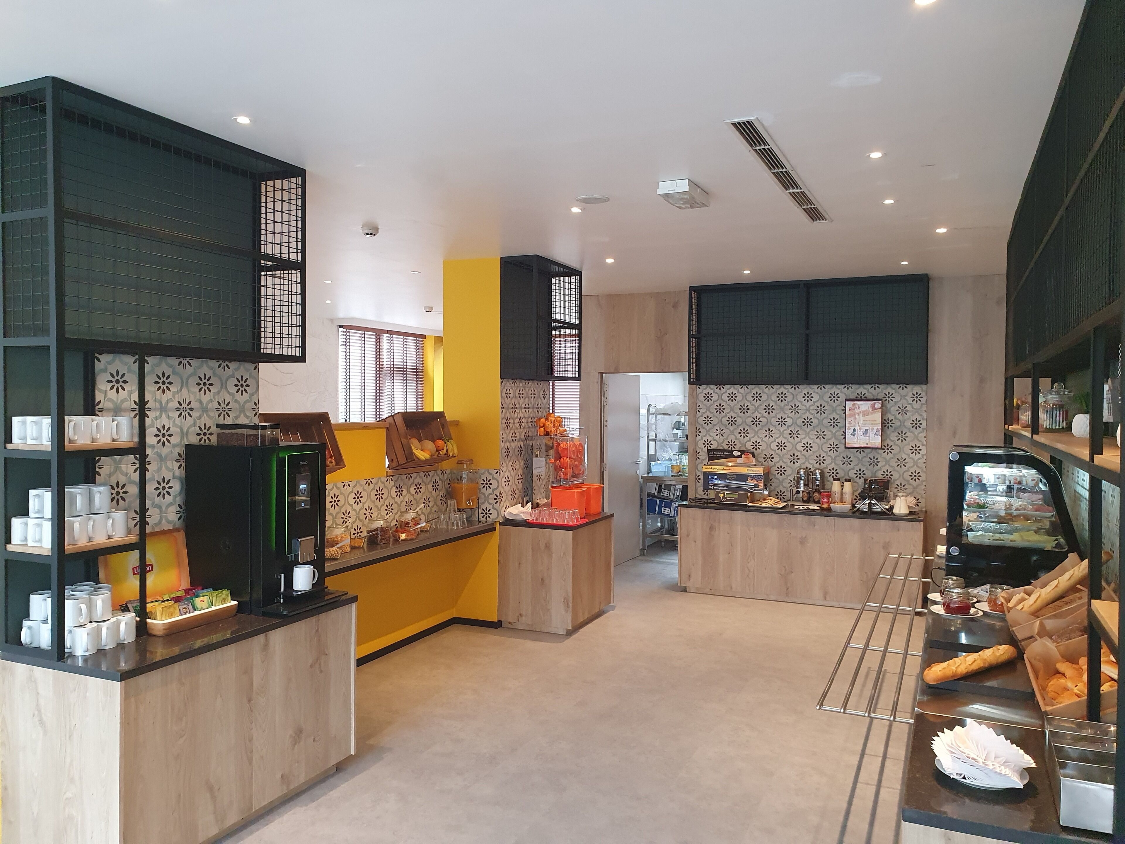 A modern cafe with a counter, shelves with cups and pastries, and a display case with food items.