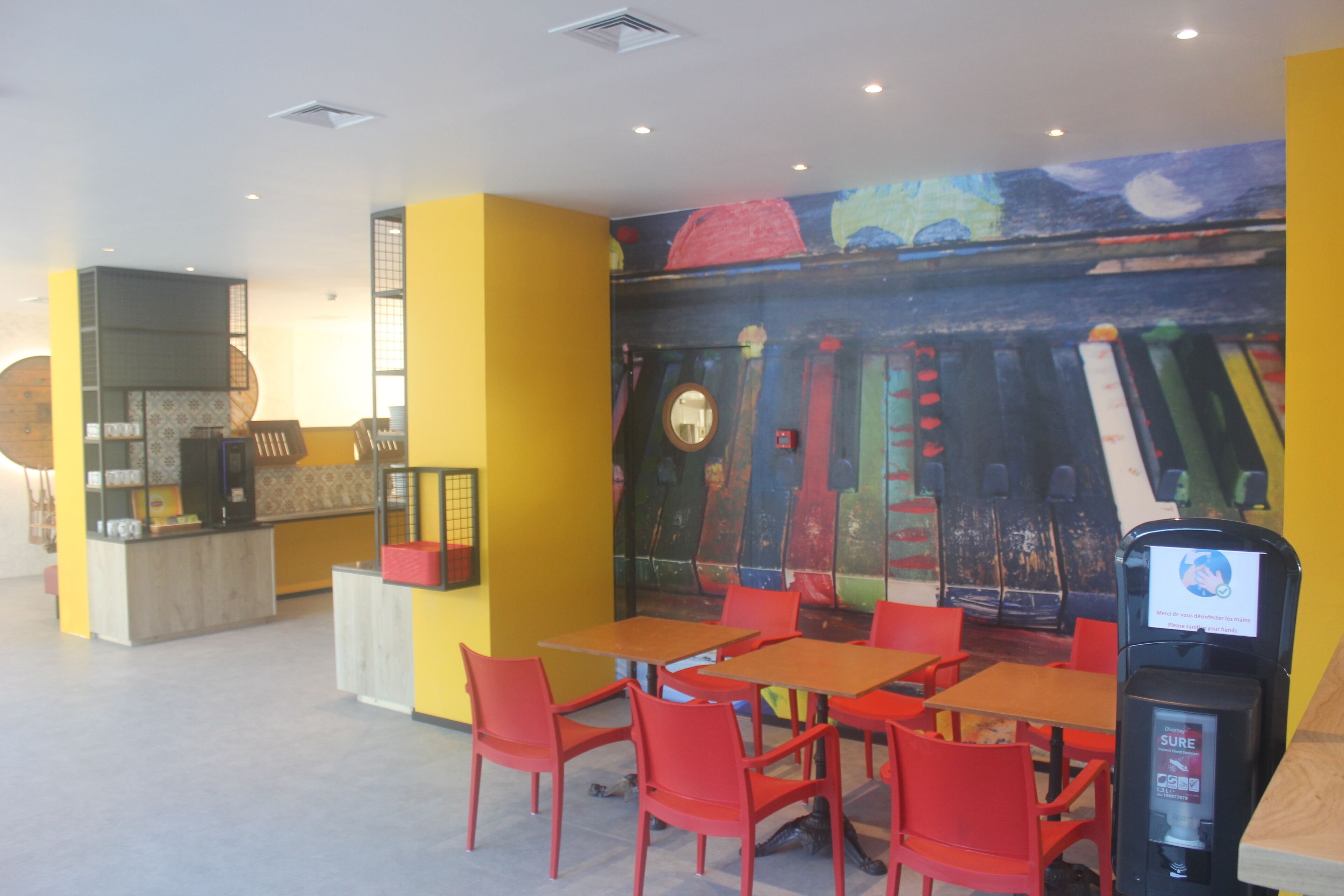 Un ristorante con sedie e tavoli rossi, un bancone e un murale sulla parete.
