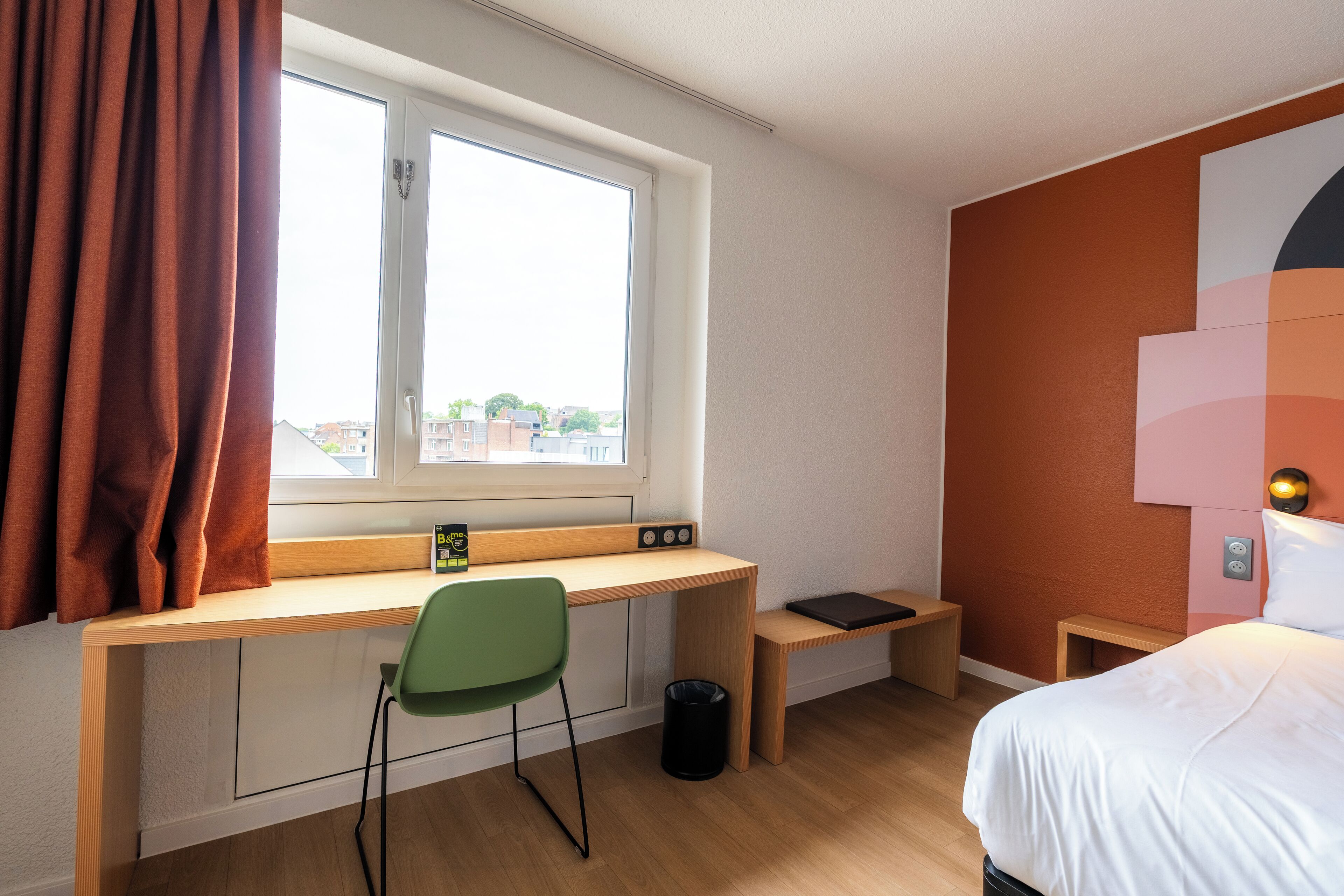Un dormitorio con un escritorio de madera, una silla verde, una cama y una ventana con cortinas.