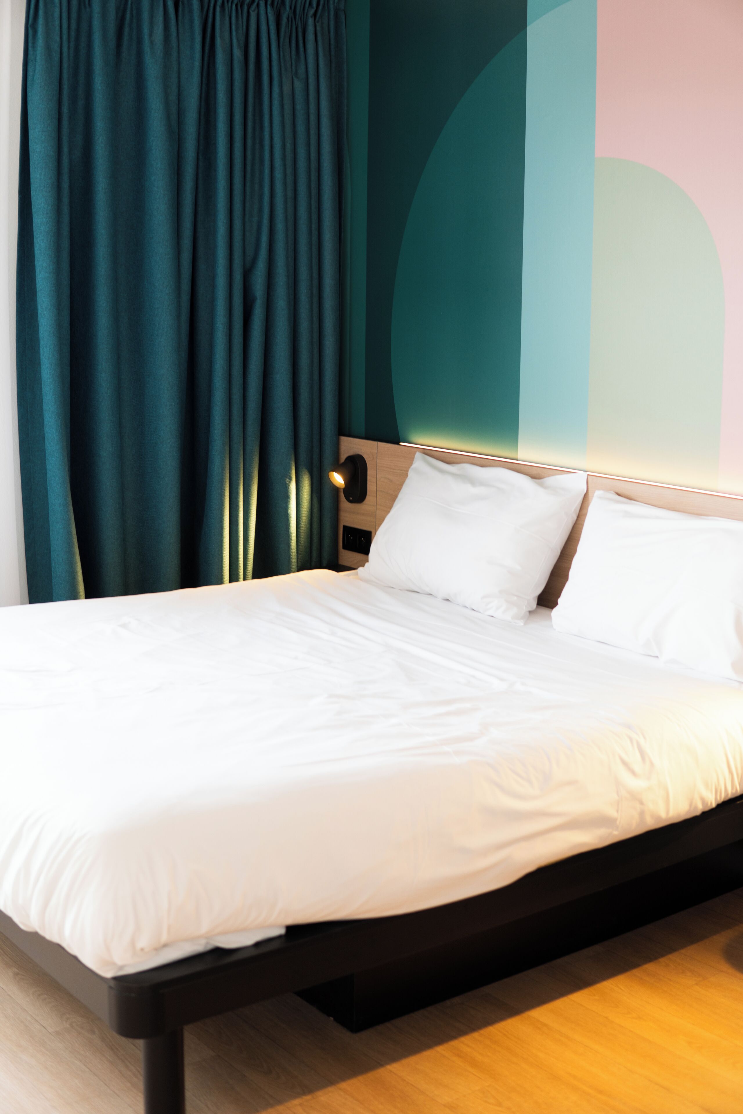 Una cama bien hecha con sábanas blancas, cabecera de madera y cortinas color turquesa.
