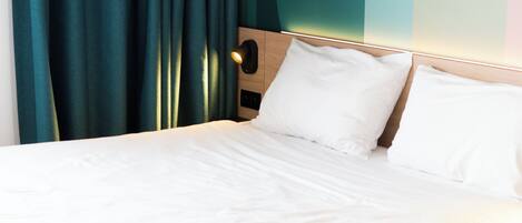 Una cama bien hecha con sábanas blancas, cabecera de madera y cortinas color turquesa.