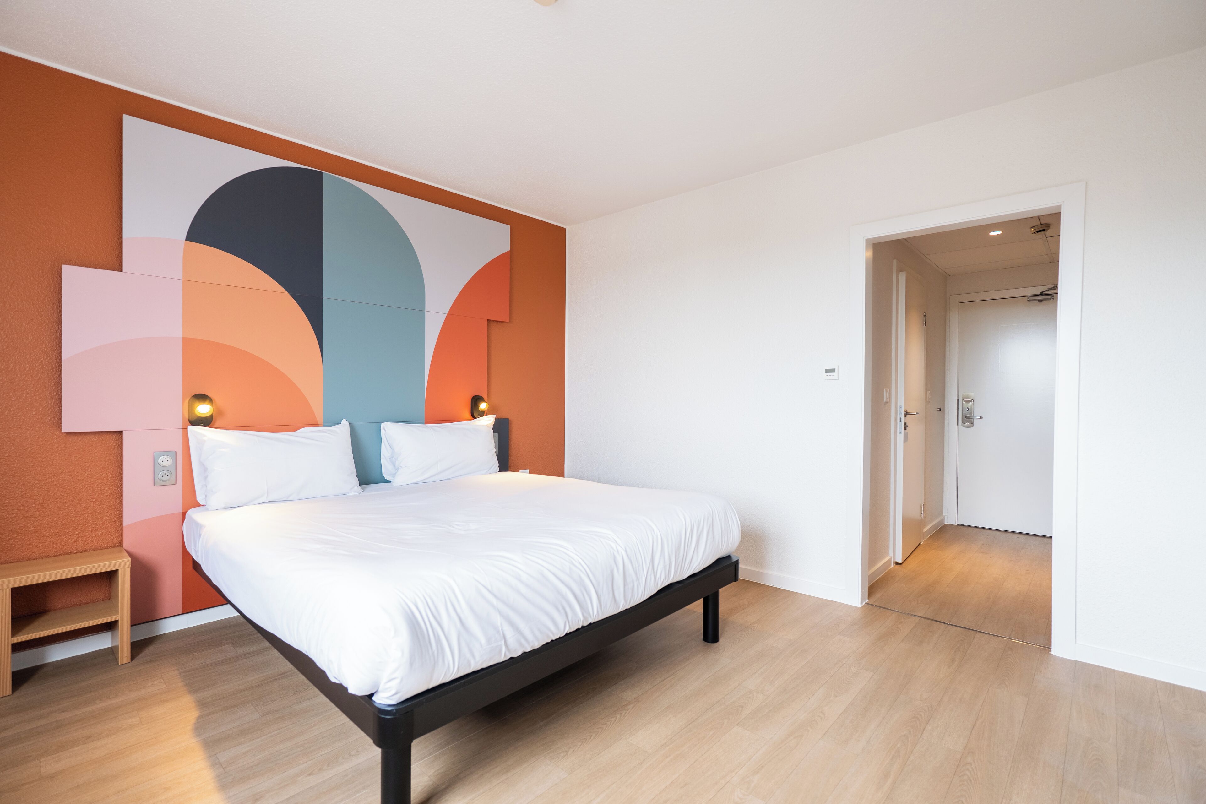 A modern bedroom with a large bed, a nightstand, and a wall art piece.