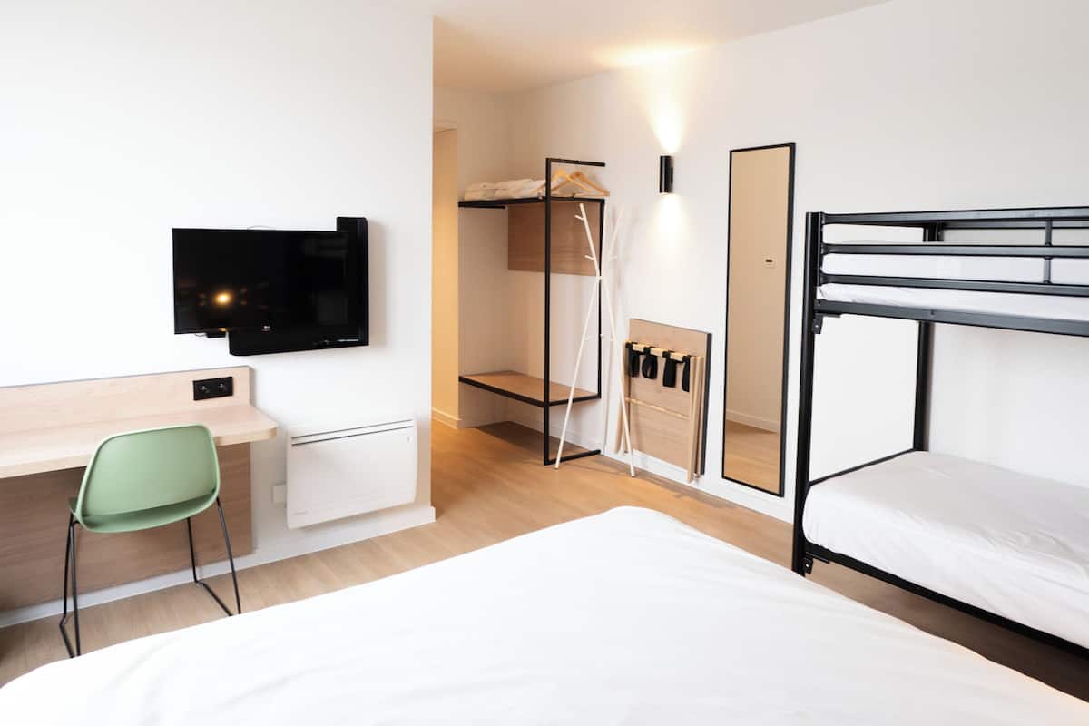 A modern hotel room with a bunk bed, a desk with a chair, a flat-screen TV, a mirror, and a wardrobe.