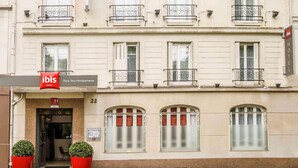 La façade d’un hôtel, avec une enseigne indiquant « Ibis Hotels Paris Tour Montparnasse » et des fenêtres numérotées.