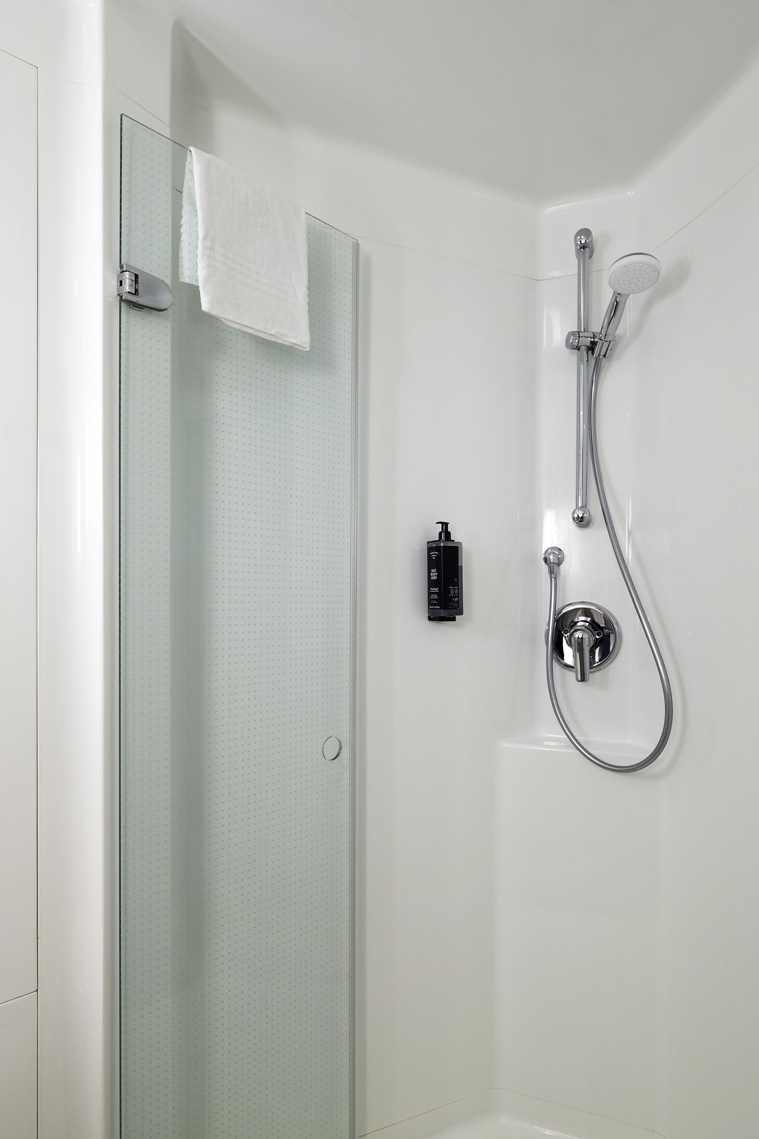 Une salle de bain moderne dotée d’une cabine de douche en verre, d’un pommeau de douche à main et d’un panneau de commande fixé au mur.