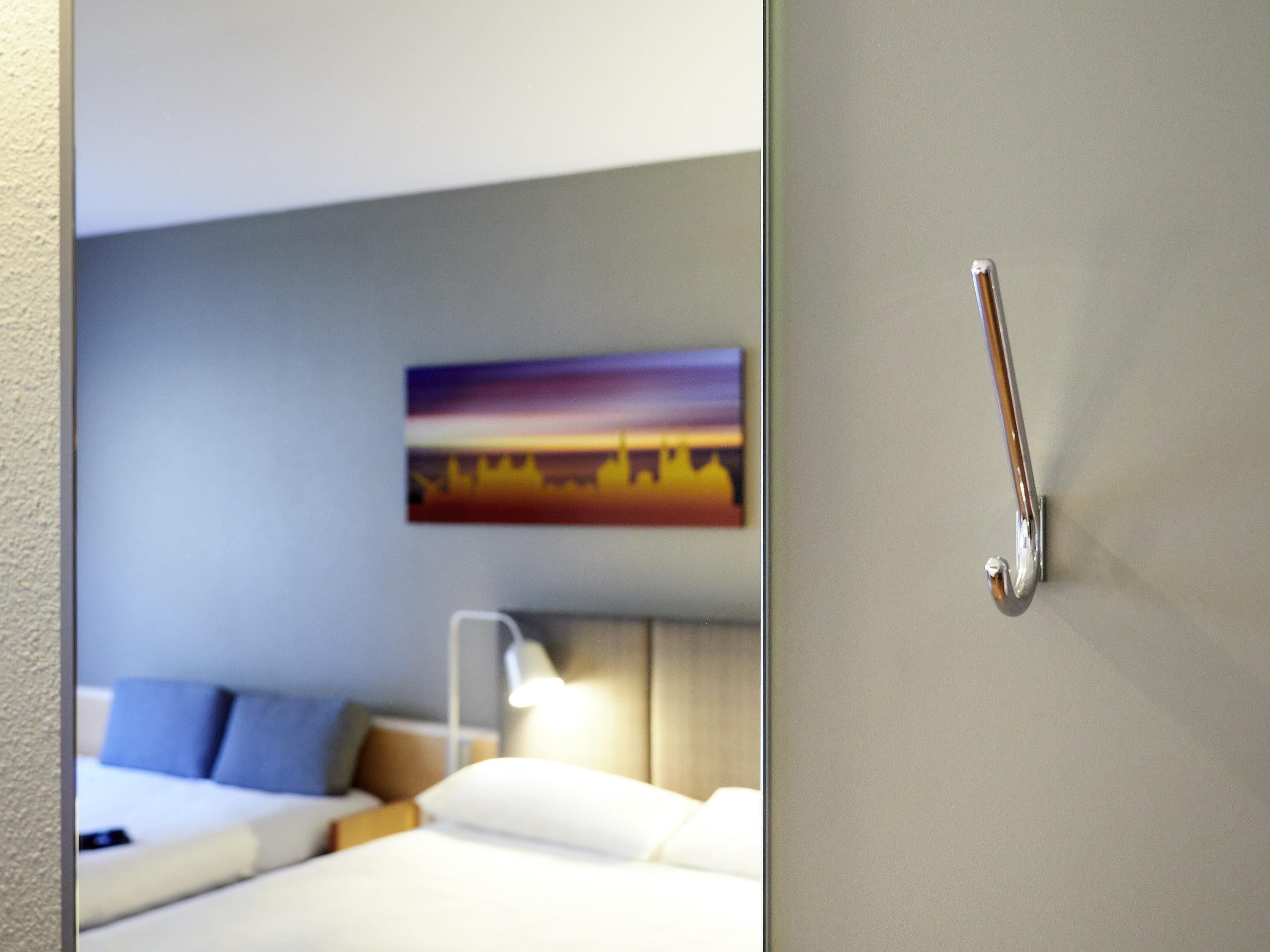A hotel room with a bed, pillows, a nightstand, a lamp, and a painting on the wall.