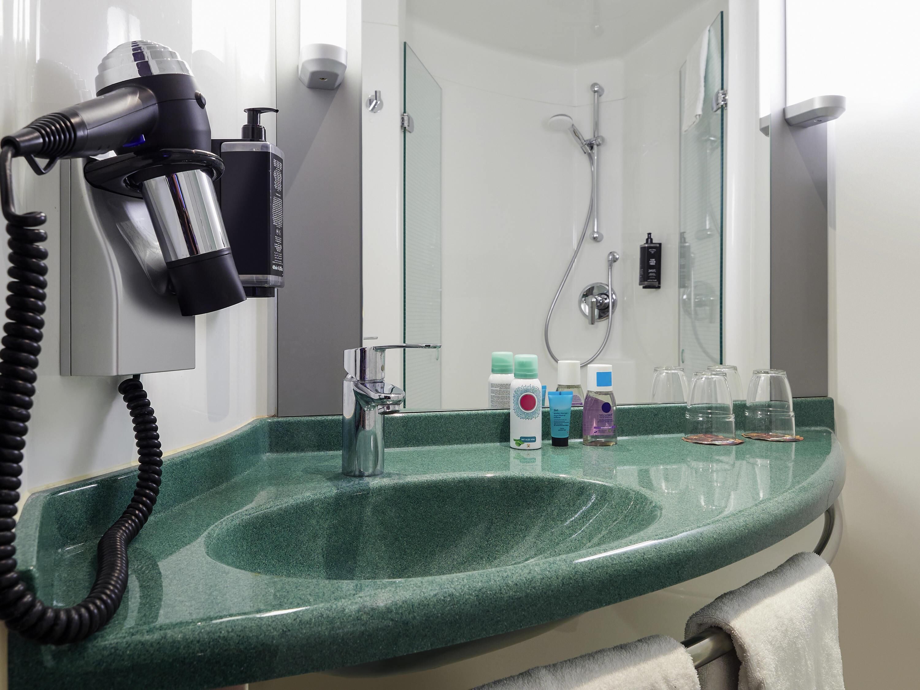 Een badkamer met een groen wastafel, een haardroger, een douche en diverse toiletartikelen.