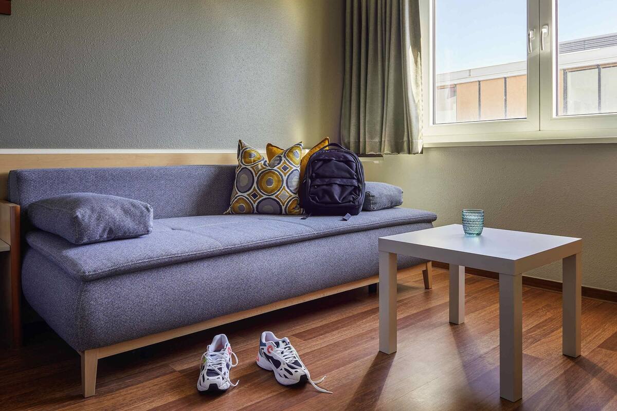 Une pièce moderne avec un canapé gris, une petite table et une fenêtre avec des rideaux.