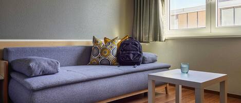 A modern room with a grey sofa, a small table, and a window with curtains.