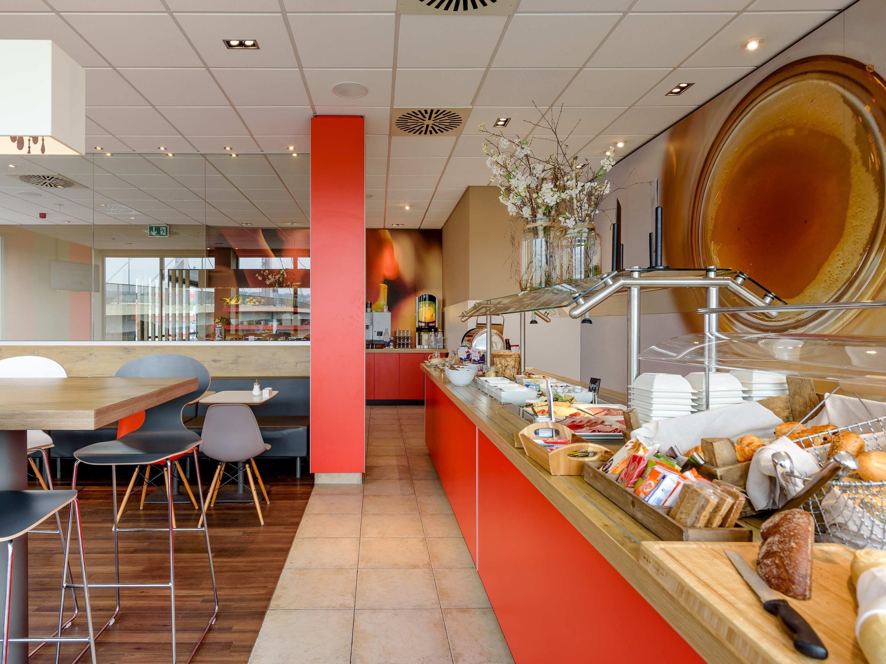 A modern cafe interior with a counter displaying food items, seating area with stools, and a decorative wall with a large circular design.
