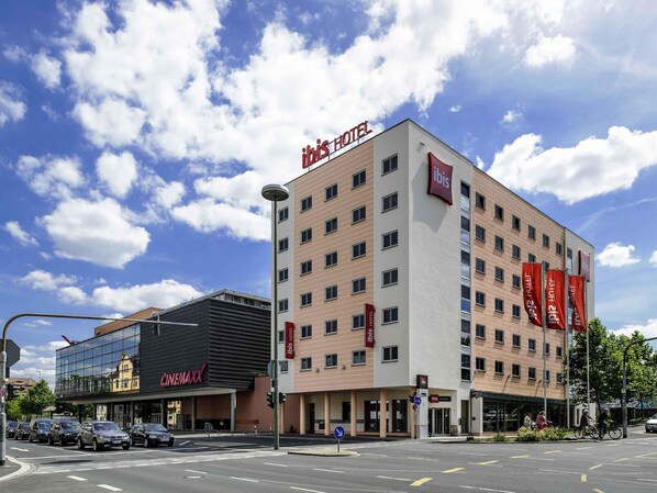Een hotel met een moderne gevel, meerdere verdiepingen en een opvallend 'ibis HOTEL' bord.