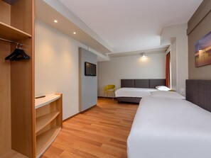 Een hotelkamer met een bed, een aan de muur bevestigde televisie, een houten garderobe en een stoel.