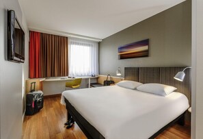 Een hotelkamer met een bed, bureau, stoel, televisie en een schilderij aan de muur.