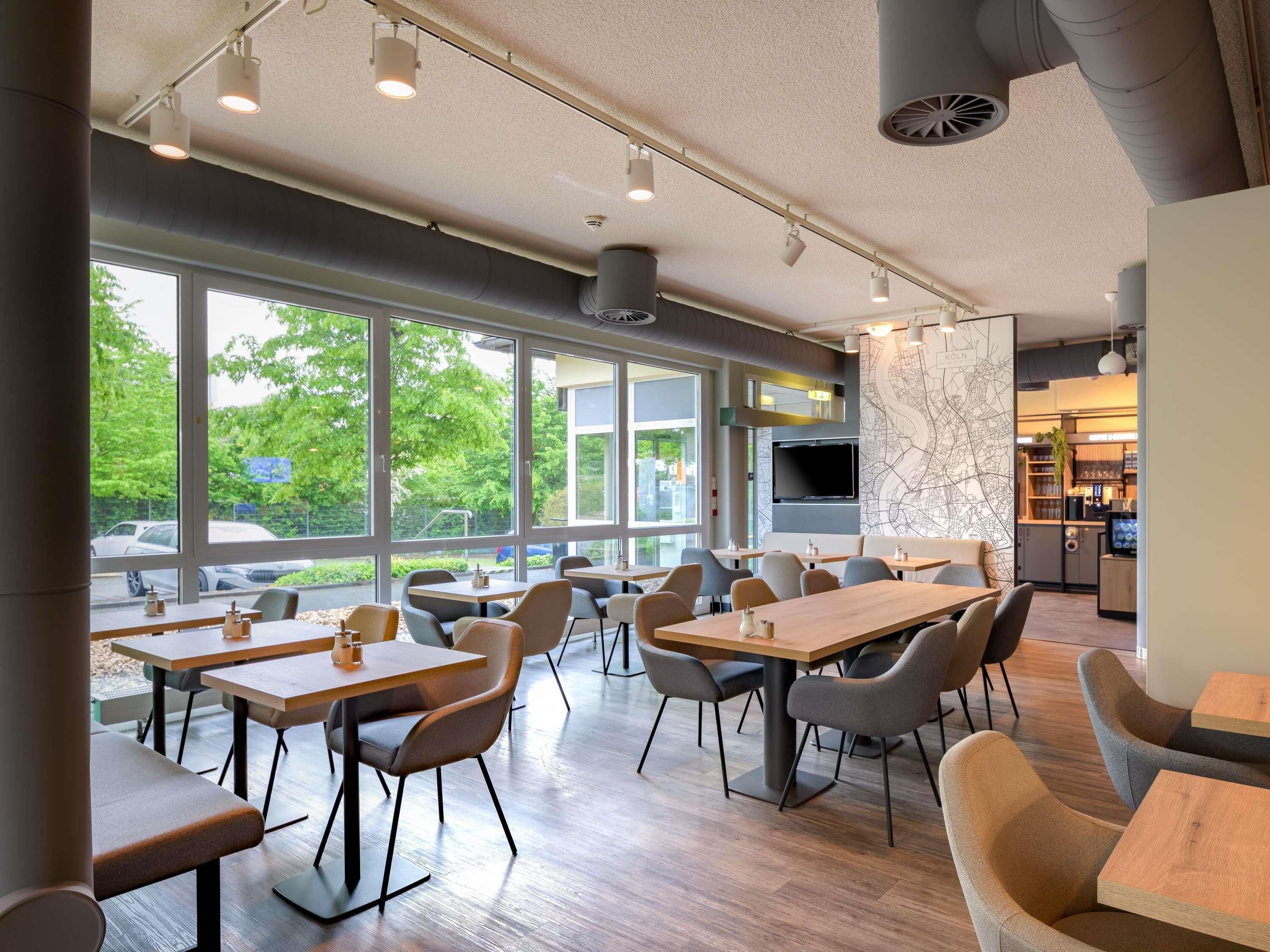 A modern dining area with large windows, multiple tables, and chairs.