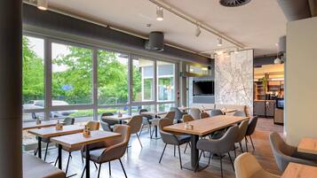 A modern dining area with large windows, multiple tables, and chairs.