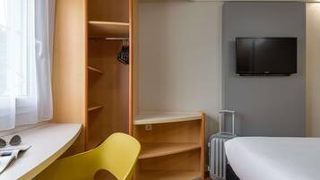 A hotel room with a bed, a desk, a chair, a wardrobe, a suitcase, and a TV.